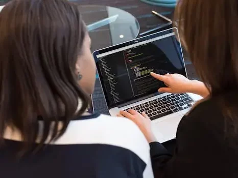 Two women working together on software programming indoors, focusing on code.